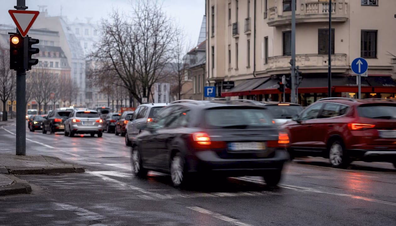 Prometna ulica v središču Ljubljane, kjer se prepletajo avtomobili, pešci in številni prometni znaki.