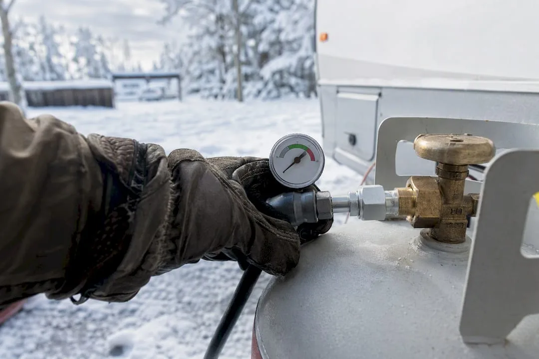 Hand checking a pressure gauge on a propane cylinder outdoors